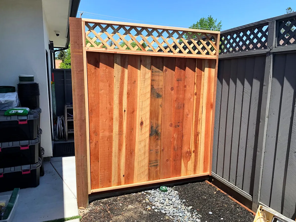 New redwood gate with a lattice top between a dark painted fence and a house wall
