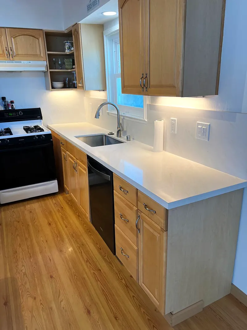 Galley kitchen run with white quartz counters, under-cabinet lights and light wood cabinets