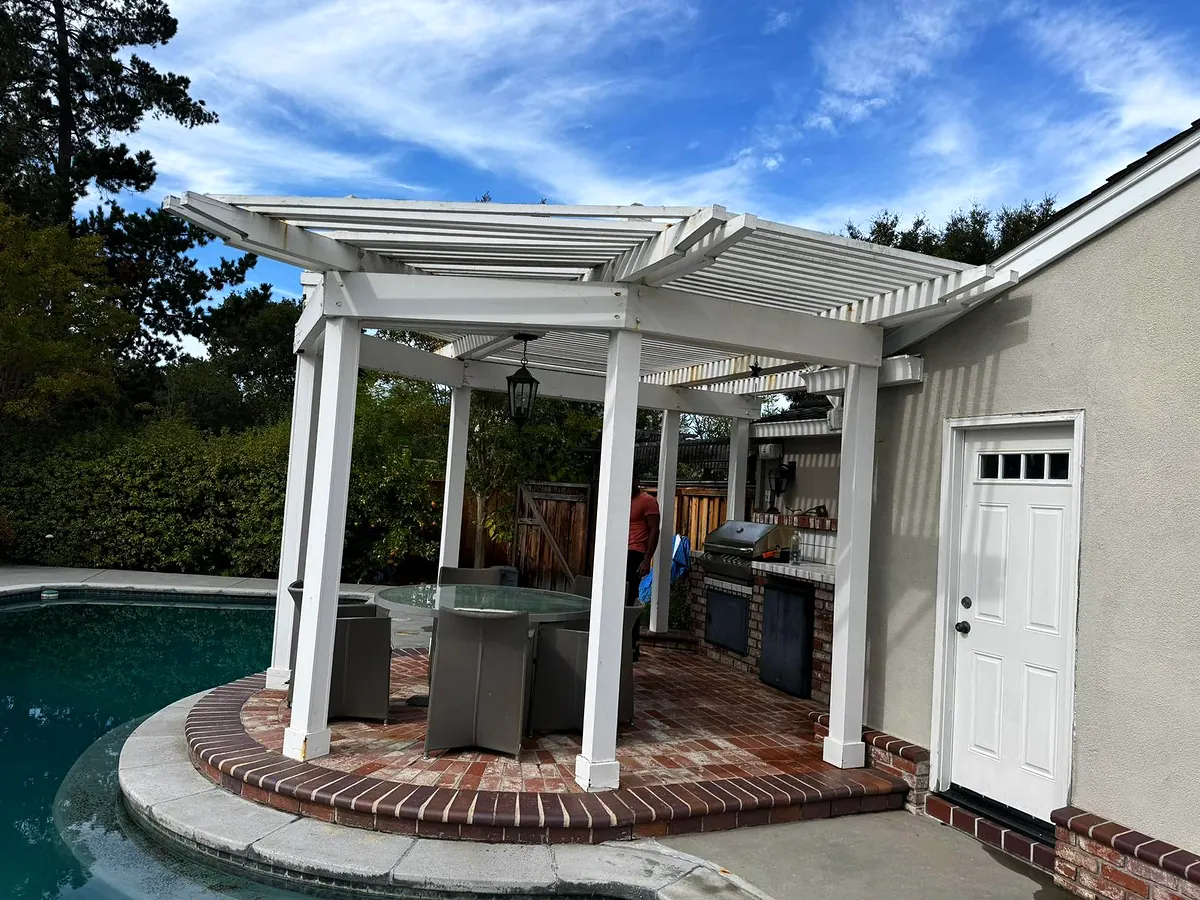 White pergola over a poolside patio next to a stucco house