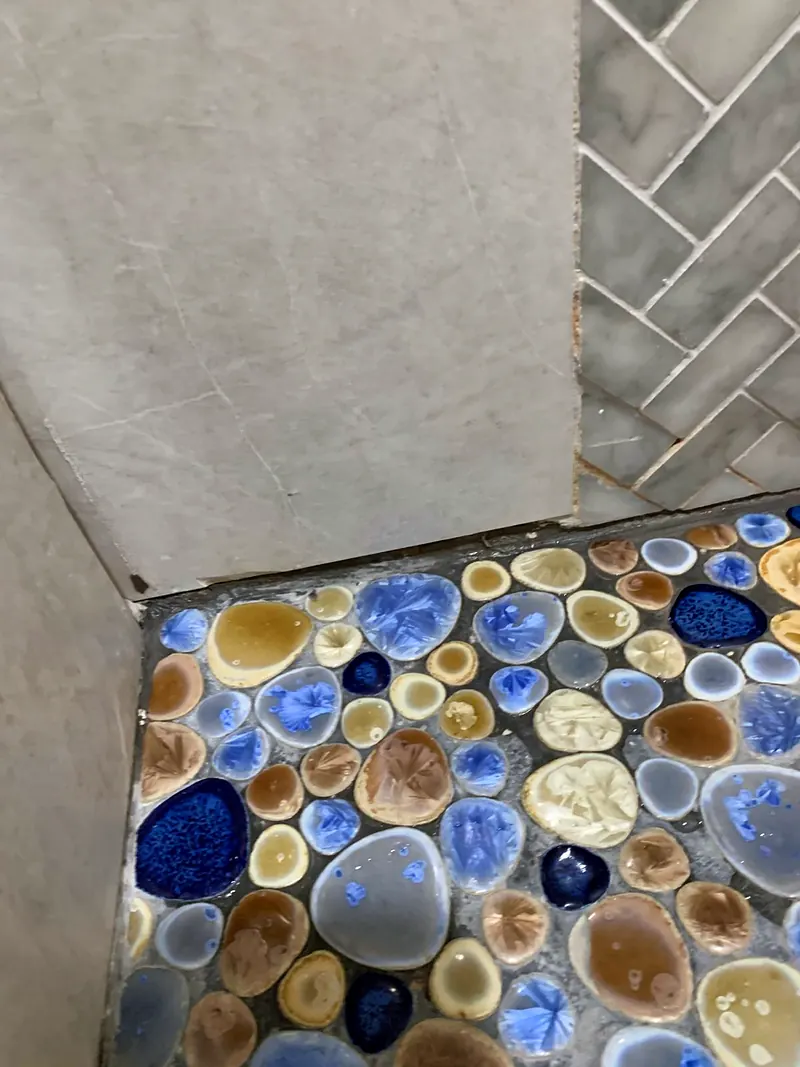 Shower floor of blue and amber glazed pebble tile meeting gray marble-look wall tile